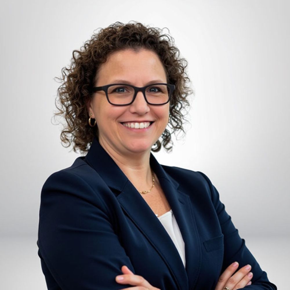 Smiling woman in a business suit, arms crossed, standing against a plain background.