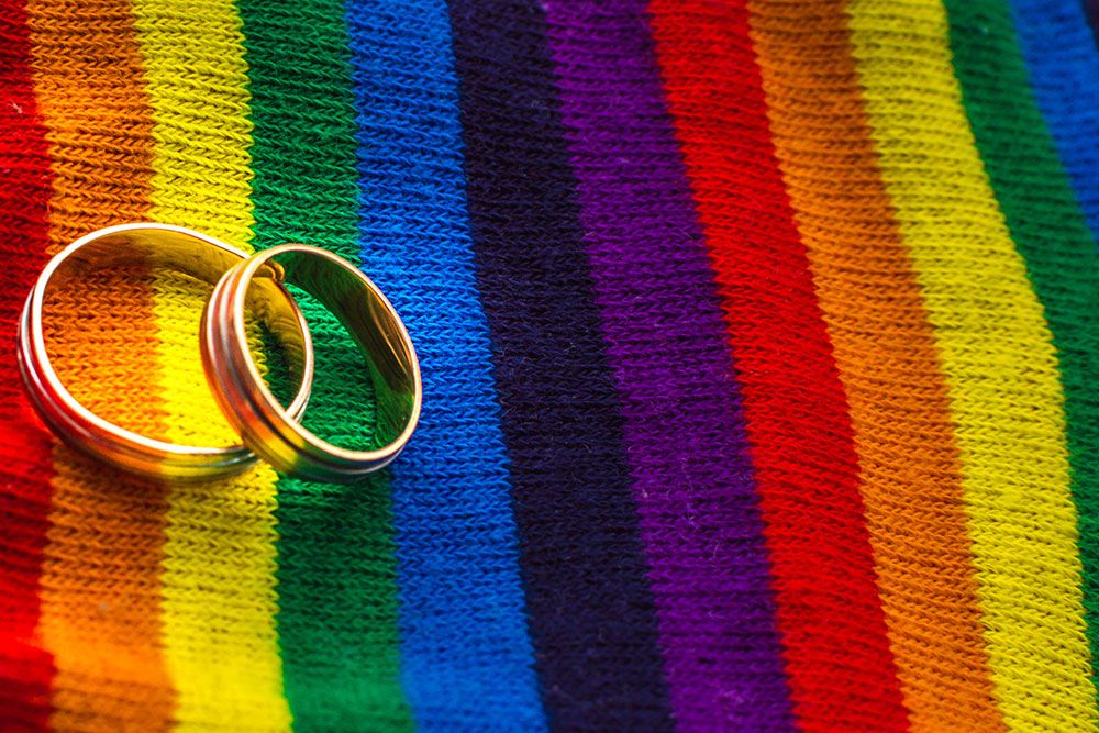 Two wedding rings on a vibrant rainbow-striped fabric, symbolizing LGBTQ+ pride and unity.