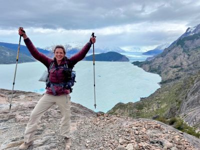 Person celebrating with hiking poles on a rocky cliff overlooking a lake and mountains.