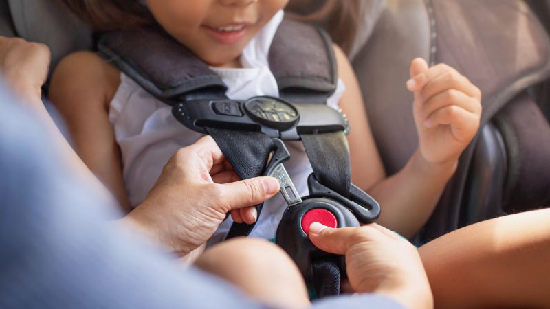 Parent buckling her child's seat belt in the car. Transportation safety.
