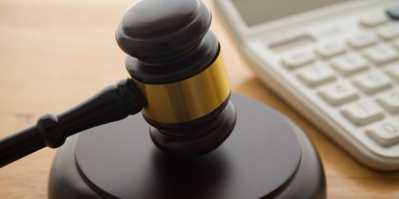 Gavel on wooden table next to a calculator, symbolizing legal and financial decisions.