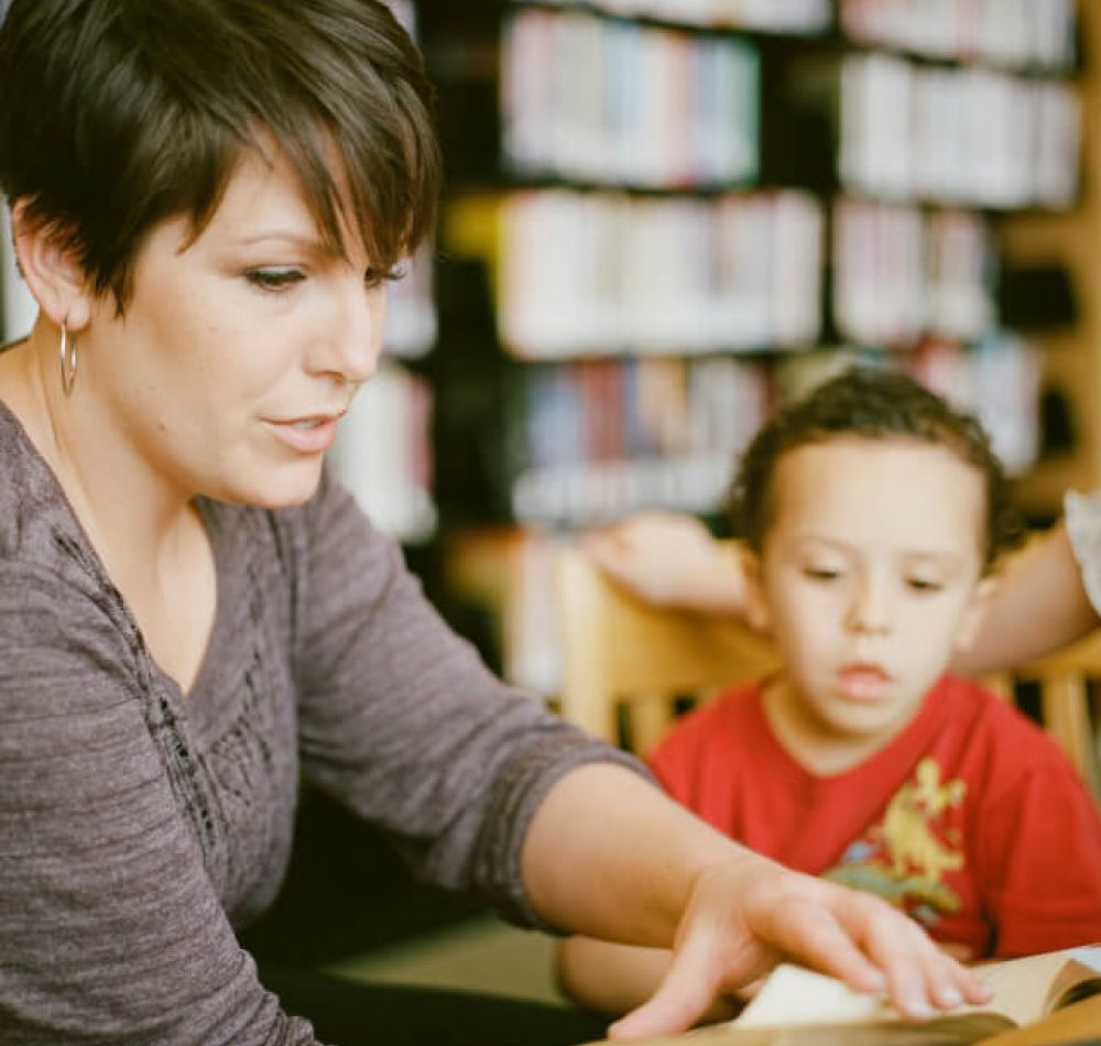 Woman reading to a child in a library, fostering learning and education.
