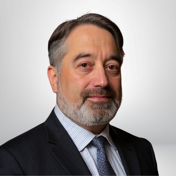 Portrait of a businessman with a beard in a suit and tie, posing against a plain background.