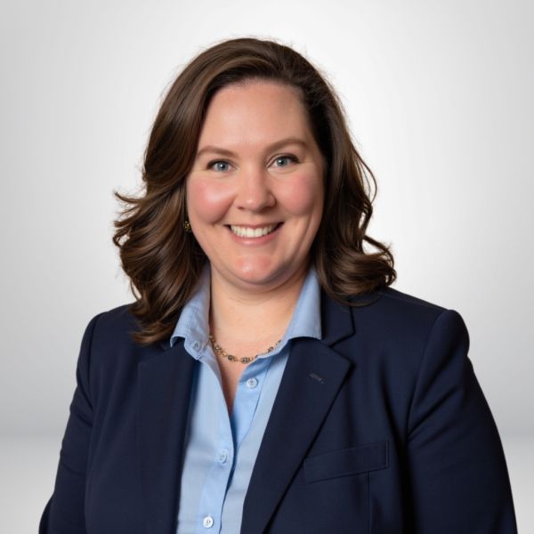 Smiling woman in a blue blazer and shirt with curly hair, posed against a light gray background.