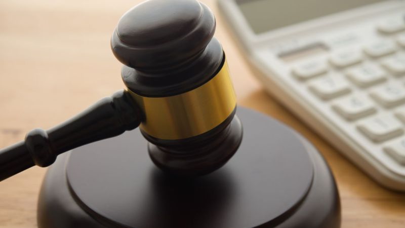 Gavel on wooden table next to a calculator, symbolizing legal and financial decisions.