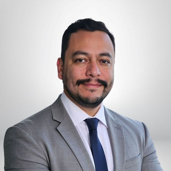 Smiling man in a gray suit and dark tie with a light background. Professional headshot.