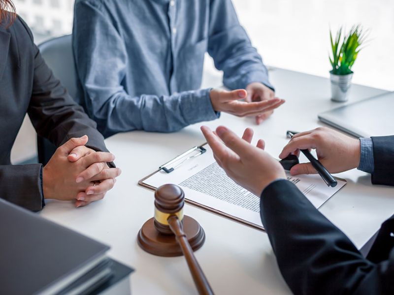 Legal consultation meeting with documents and gavel on table, two people discussing with lawyer in office.