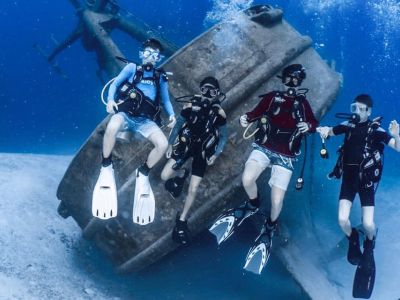 Four scuba divers explore a sunken shipwreck underwater.