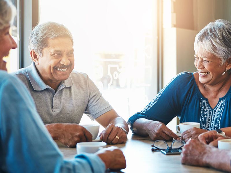 Senior friends laughing and enjoying coffee together at a cafe, sunlight streaming in through the window.
