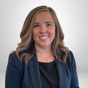 Smiling businesswoman in a black blazer, light background.