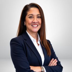 Businesswoman in a navy blazer smiling with arms crossed against a neutral background.