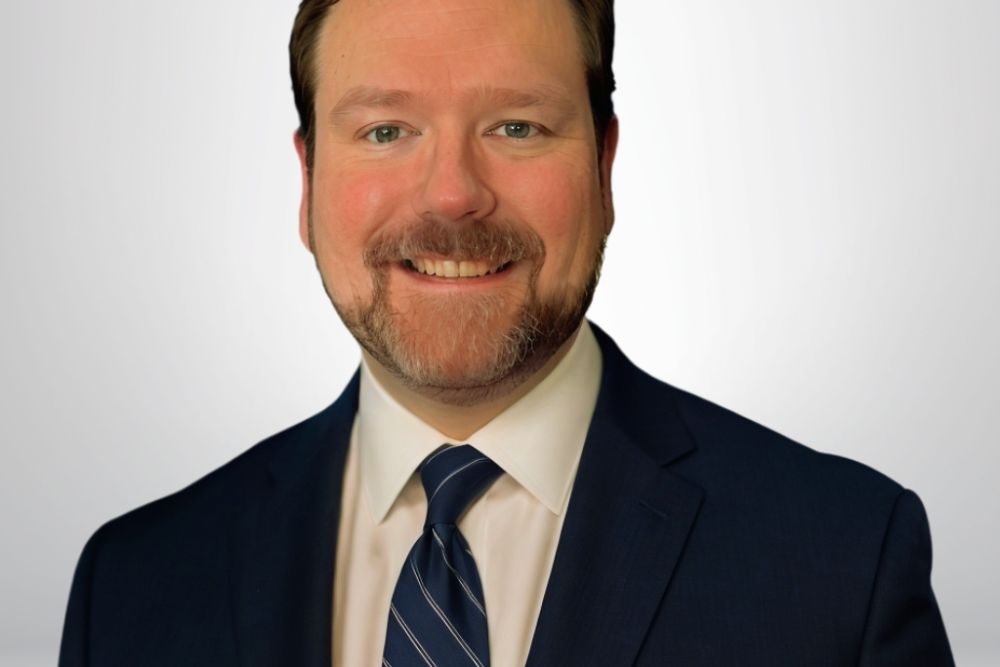 A smiling man in a suit and tie against a plain background.