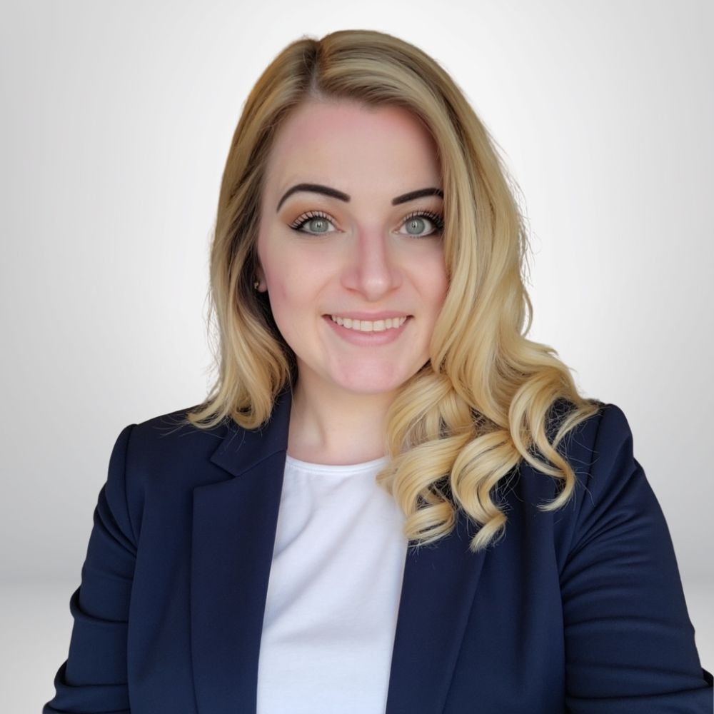 Portrait of a smiling woman with blonde hair in a navy blazer, professional appearance, on a neutral background.