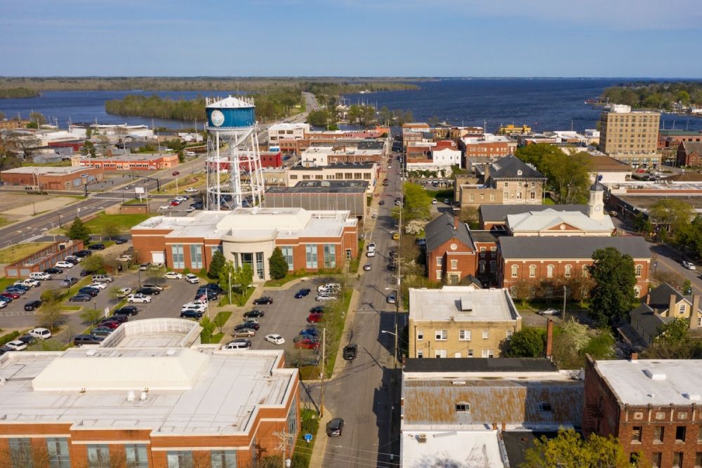 Aerial view of a small lakeside town with a prominent water tower, surrounded by buildings and roads.