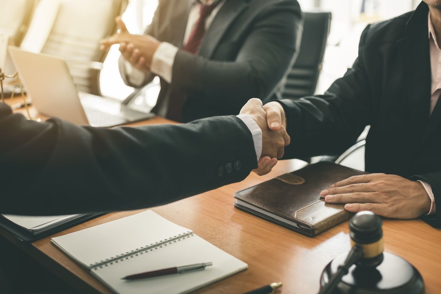 Business meeting with two professionals shaking hands at a table with documents and laptops.