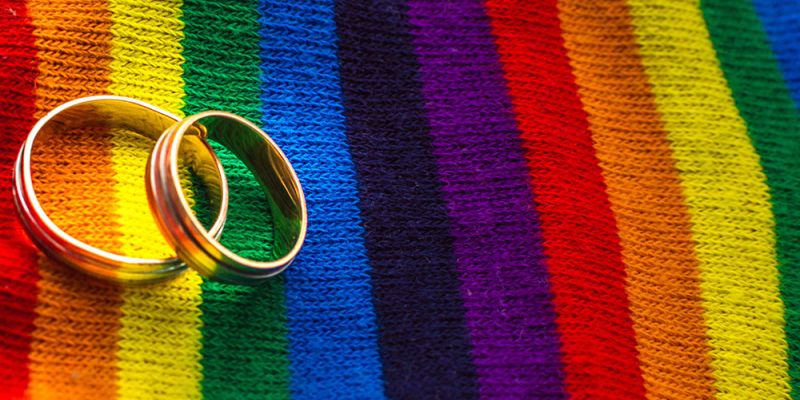 Two wedding rings on a vibrant rainbow-striped fabric, symbolizing LGBTQ+ pride and unity.
