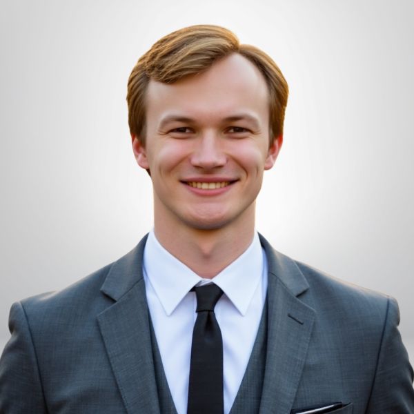 Smiling man in a grey suit and black tie, professional portrait against neutral background.