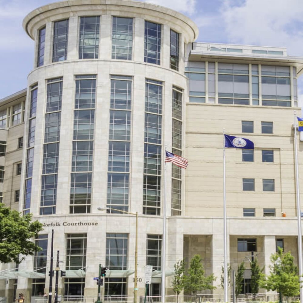 Modern courthouse building with glass facade in Norfolk, USA, featuring American and state flags under a clear sky.