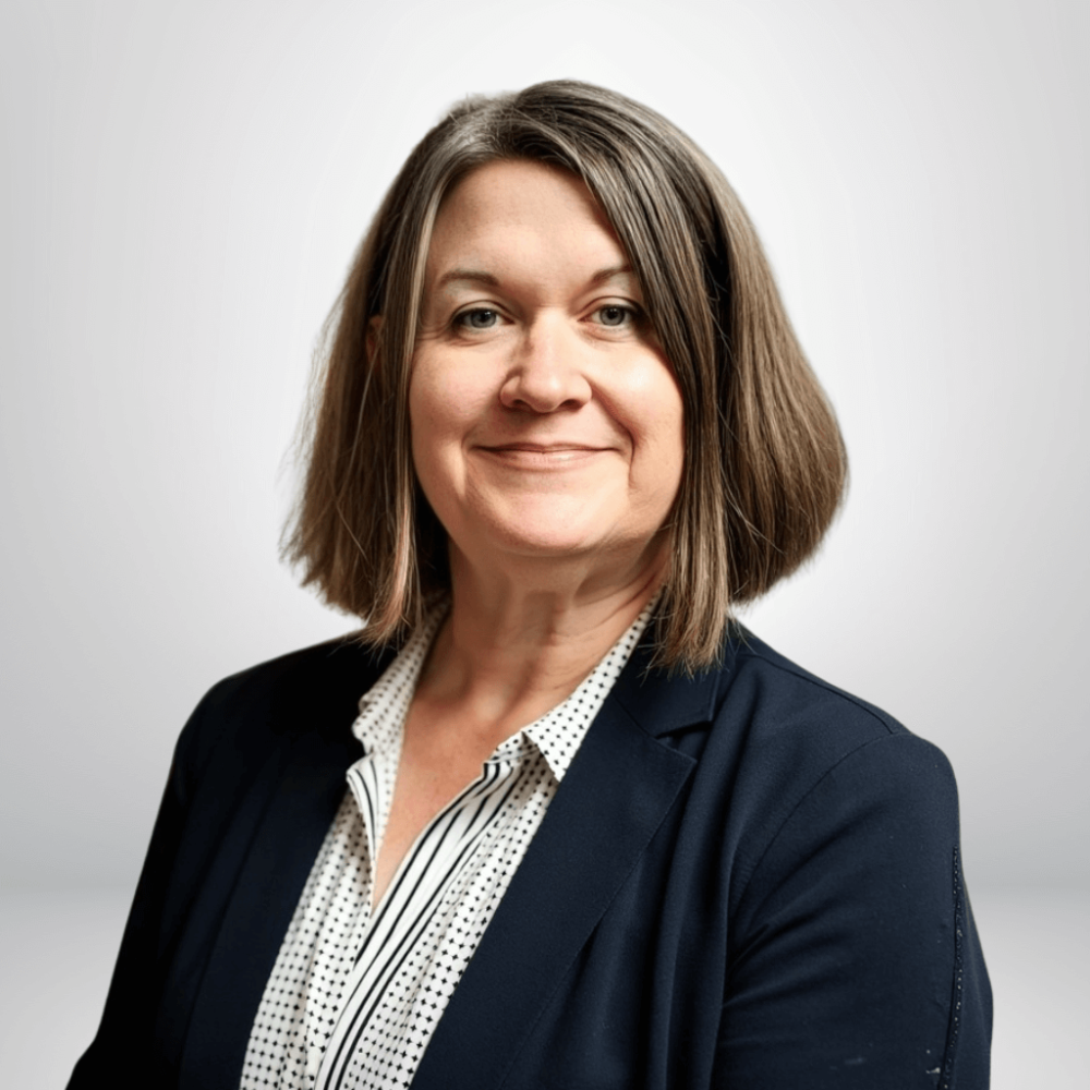 Portrait of a professional woman in a blazer, smiling against a plain background. Business attire for a corporate setting.
