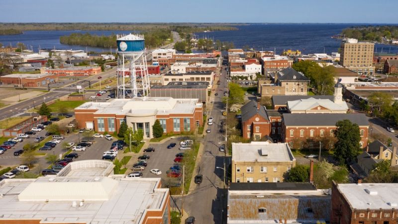 Aerial view of a small lakeside town with a prominent water tower, surrounded by buildings and roads.