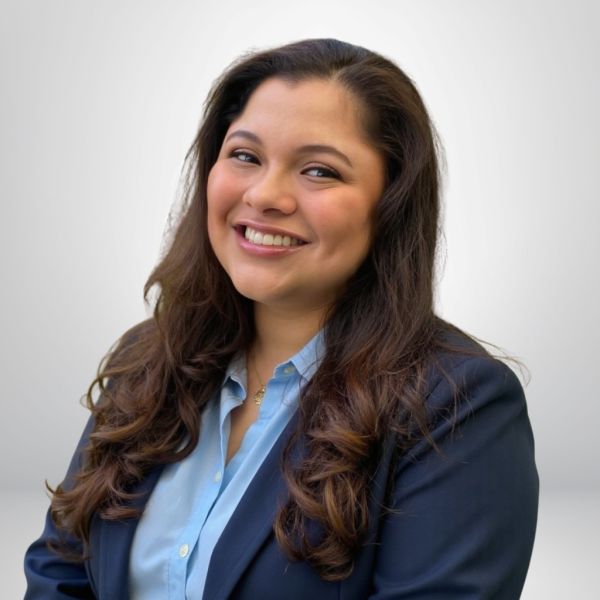 Smiling woman in a blue shirt and blazer, with long hair, posing against a simple background.