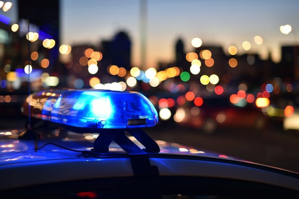 Police car with flashing blue lights in city traffic at dusk, blurred background with colorful bokeh.
