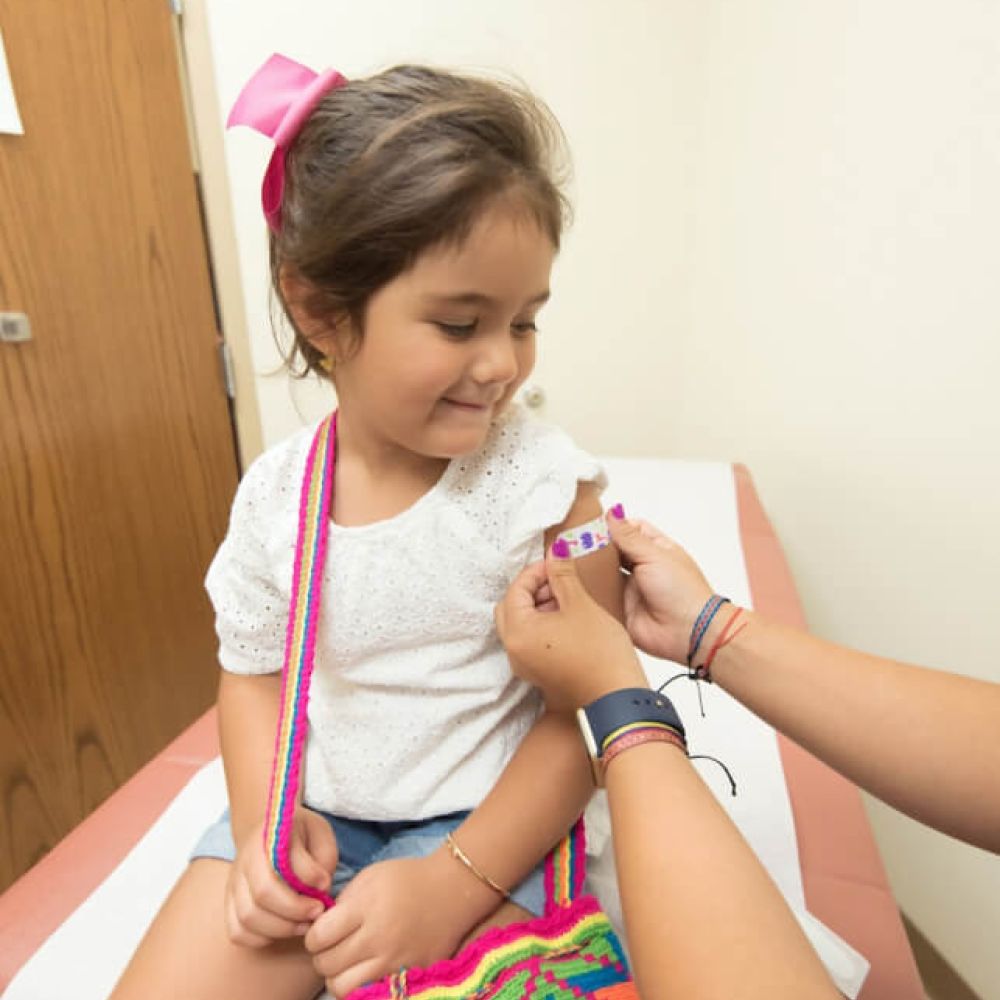 Child receiving a colorful bandage after vaccination in a doctor's office.