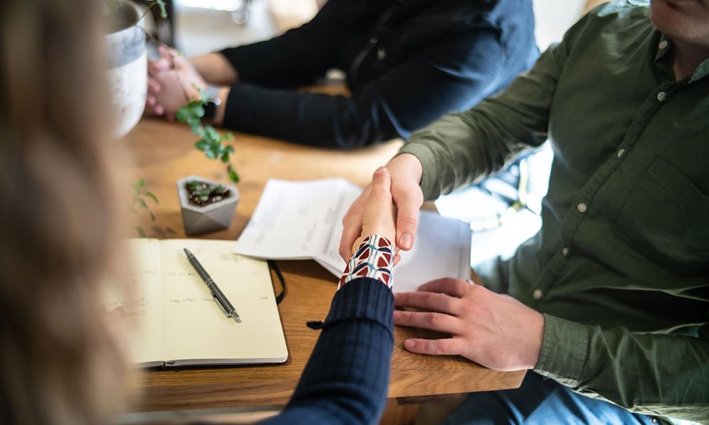 Handshake at a meeting table with notebook and documents, symbolizing business agreement or partnership.