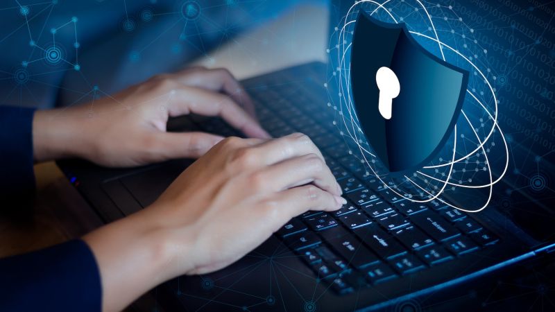 Hands typing on laptop keyboard with digital security shield overlay, representing cybersecurity and data protection.