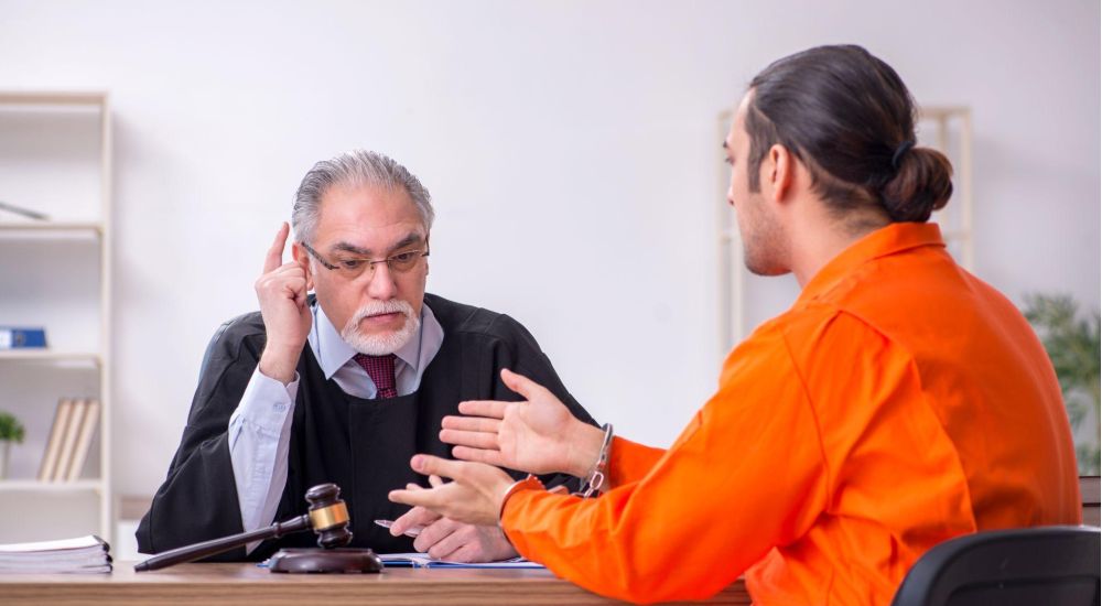 Judge listening to a prisoner in an orange jumpsuit during a courtroom discussion.