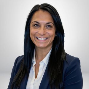 Smiling woman in business attire, with long black hair, against a neutral background. Ideal for professional profile use.