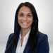 Smiling woman in business attire, with long black hair, against a neutral background. Ideal for professional profile use.