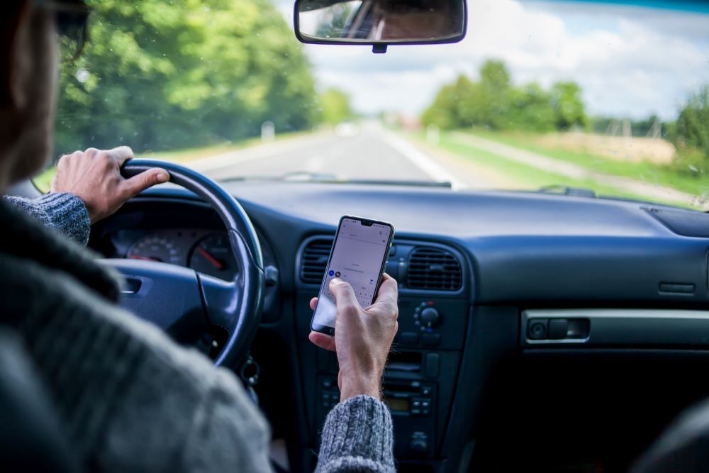Driver using a smartphone while driving on a road; distracted driving safety concern.