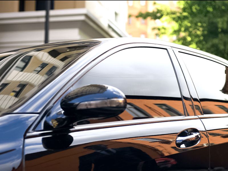 Sleek black car with tinted windows reflecting a cityscape, emphasizing luxury and urban lifestyle.