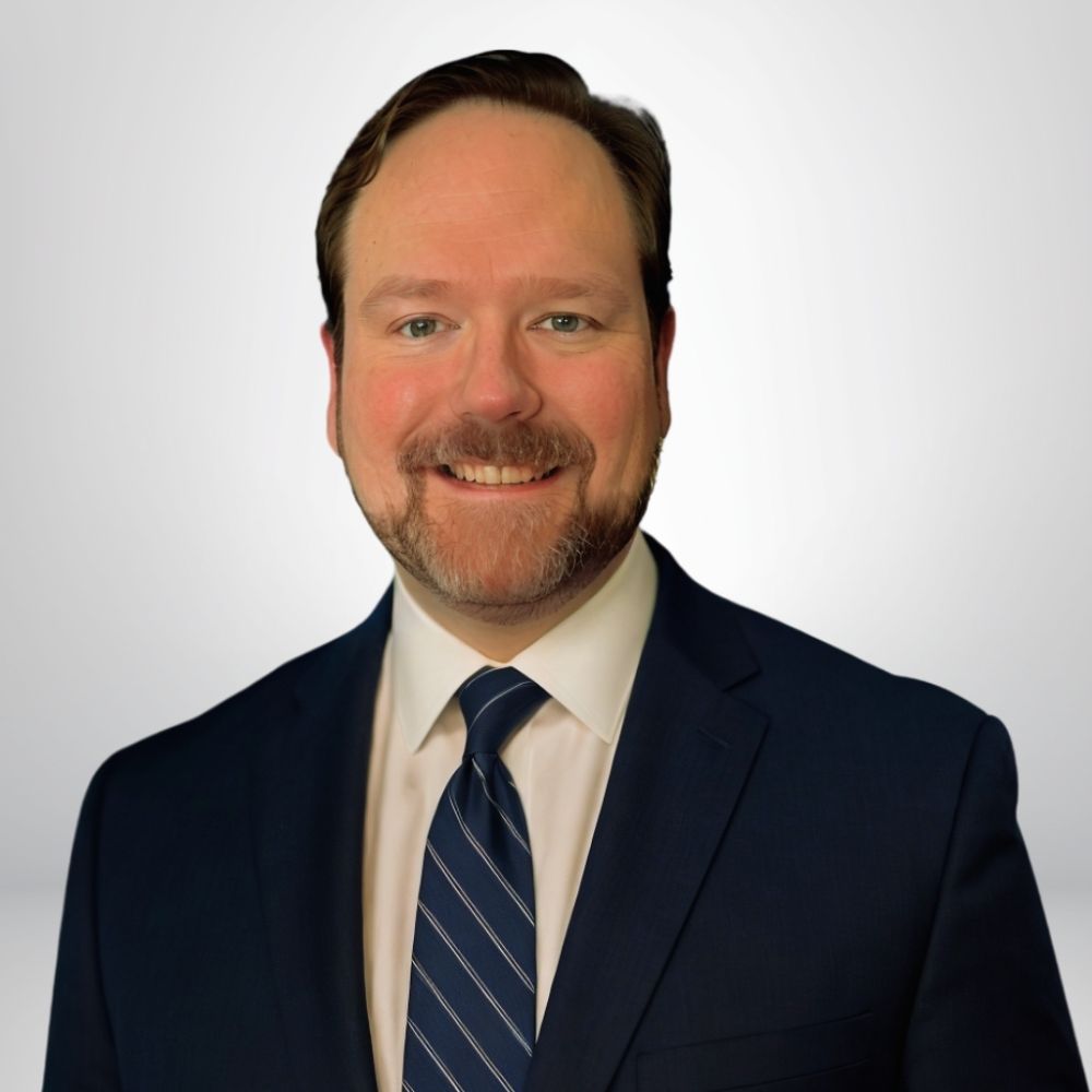 A smiling man in a suit and tie against a plain background.