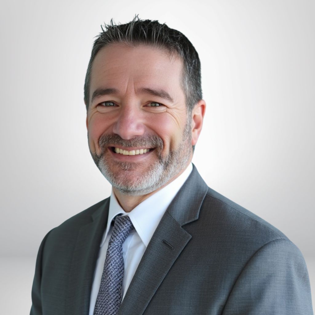 Smiling man in a business suit with a tie, against a plain background.