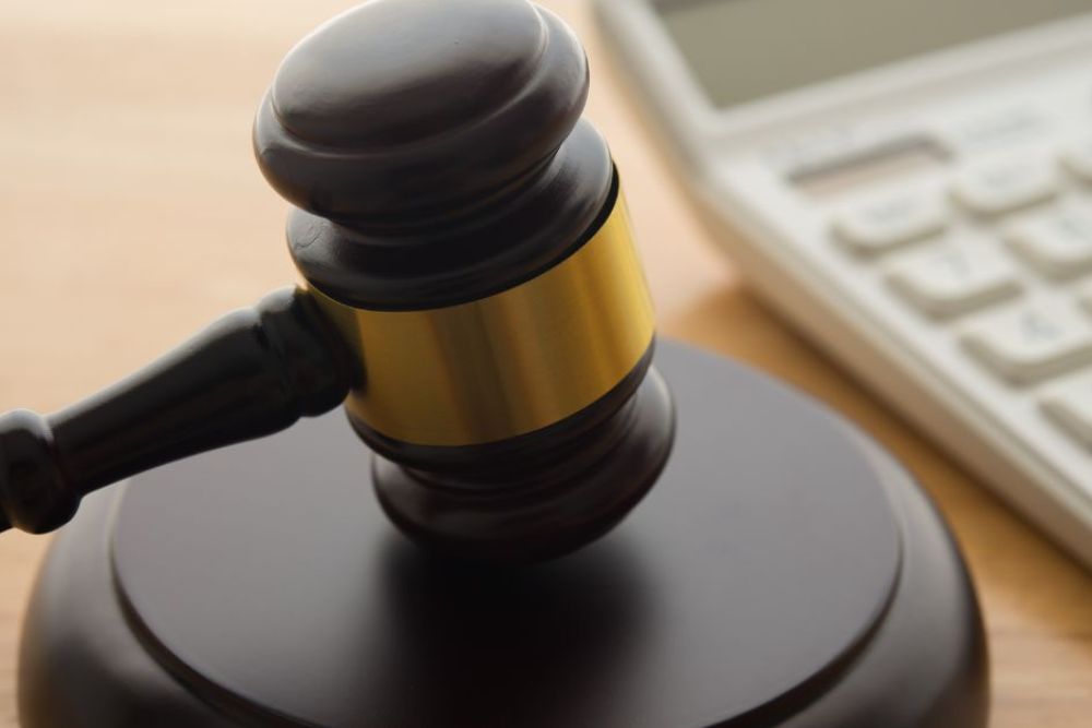 Gavel on wooden table next to a calculator, symbolizing legal and financial decisions.
