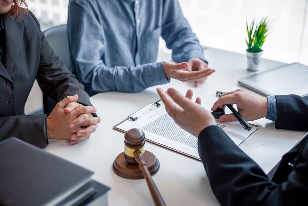 Legal consultation meeting with documents and gavel on table, two people discussing with lawyer in office.