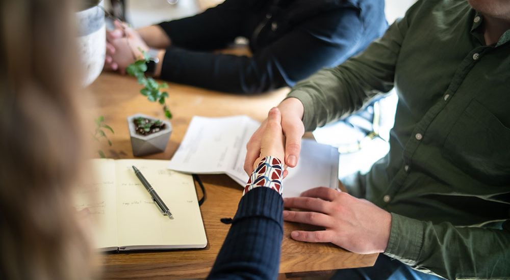Handshake at a meeting table with notebook and documents, symbolizing business agreement or partnership.