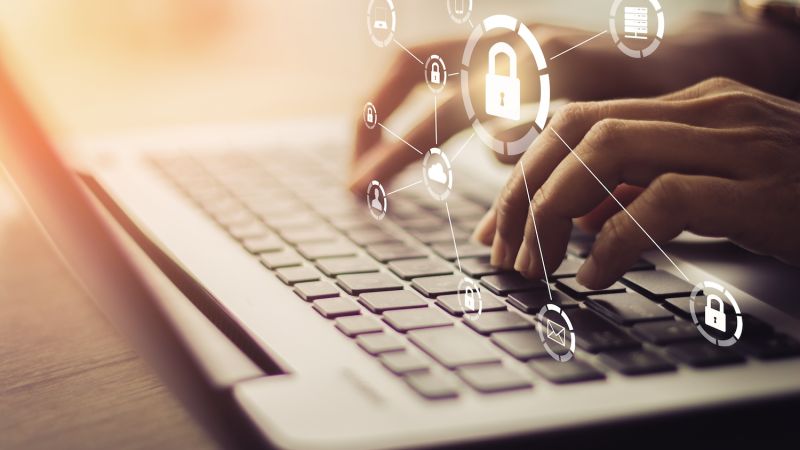 Hands typing on a laptop with digital security icons, representing online data protection and cybersecurity.