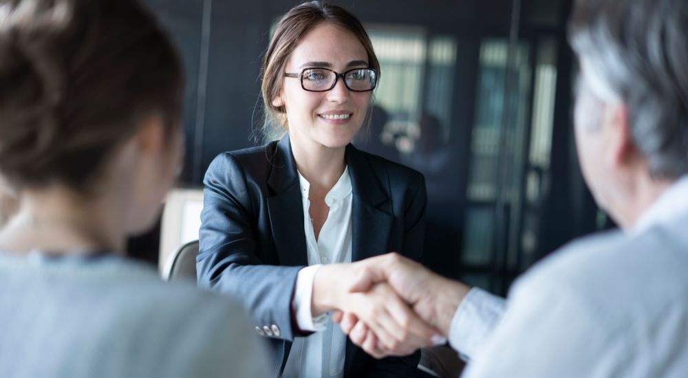Businesswoman in glasses smiling and greeting colleagues with a handshake during a meeting, symbolizing successful negotiation.