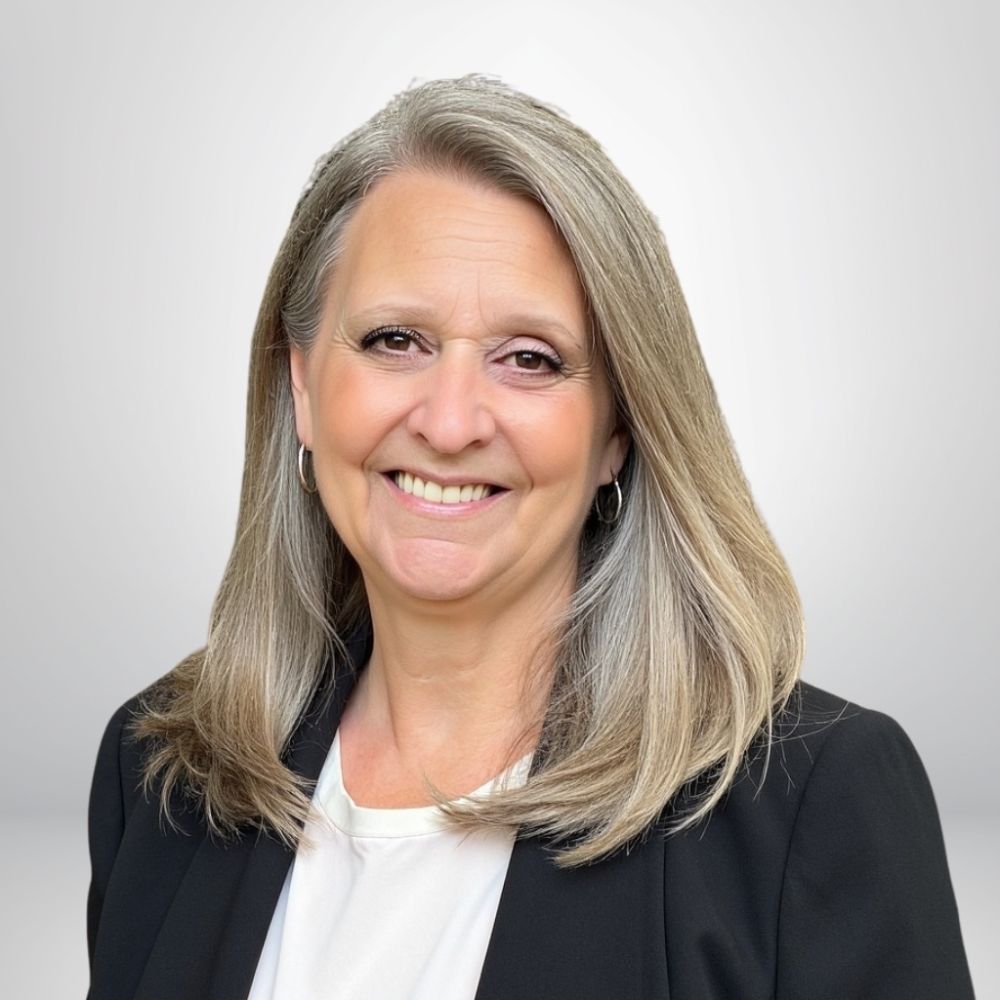 Smiling woman with long gray hair in a business jacket against a light gray background.