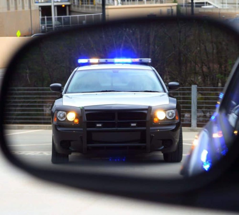 Police car with flashing lights seen in rear-view mirror on a road.