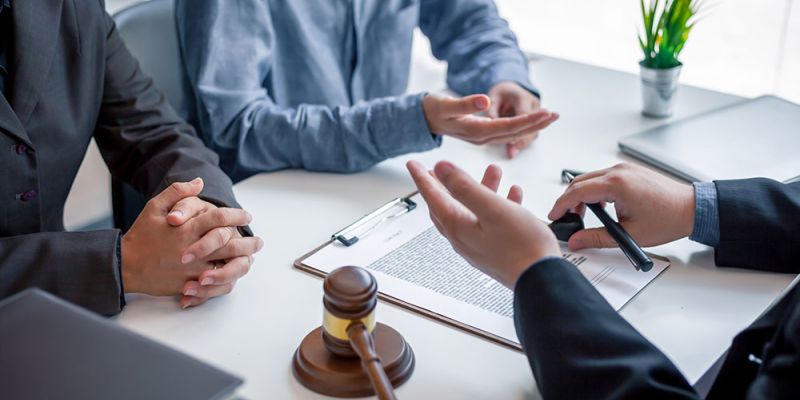 Legal consultation meeting with documents and gavel on table, two people discussing with lawyer in office.