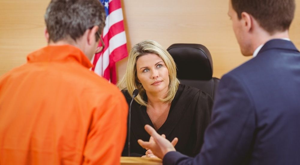 Judge attentively listening to lawyers in a courtroom discussion, with the American flag in the background.