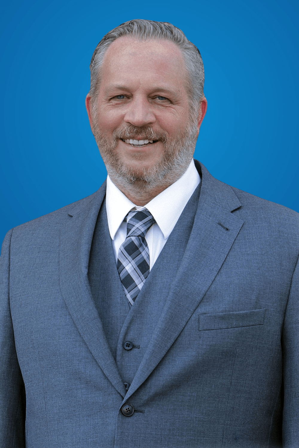 Smiling man in a blue suit and tie against a blue background.