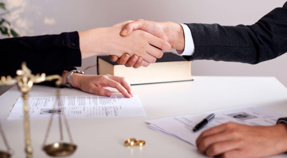 Handshake over legal documents with scales of justice in foreground, signifying agreement or legal deal.