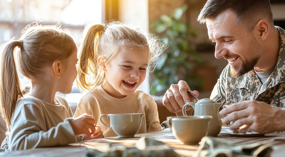 Father in camouflage uniform enjoying tea with his smiling daughters at home.