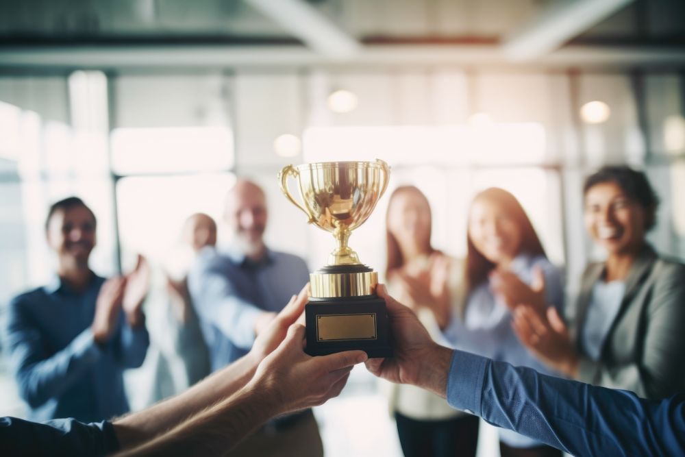 Team celebrating with trophy, applauding success and achievement in a bright office setting.