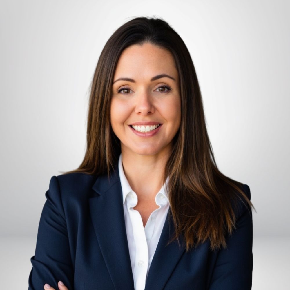 Professional woman smiling in business suit with arms crossed against neutral background.